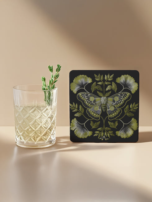 Square black ceramic coaster featuring a detailed chartreuse luna moth illustration surrounded by symmetrical botanical elements including ginkgo-inspired leaves and delicate foliage.